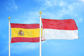 Spain and Indonesia two flags on flagpoles and blue cloudy sky