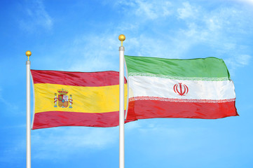 Spain and Iran two flags on flagpoles and blue cloudy sky