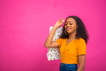 beautiful african lady isolated over pink background feeling excited as she is holding shopping bag.