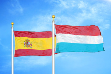 Spain and Luxembourg two flags on flagpoles and blue cloudy sky