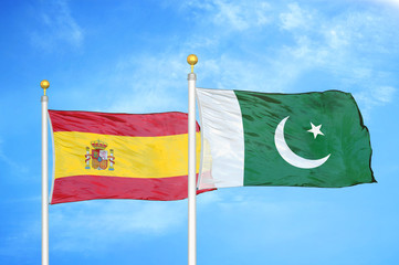 Spain and Pakistan two flags on flagpoles and blue cloudy sky