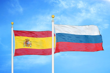 Spain and Russia two flags on flagpoles and blue cloudy sky