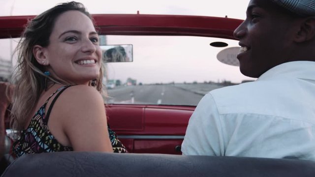Young man and woman sitting in convertible and dancing, enjoying road trip