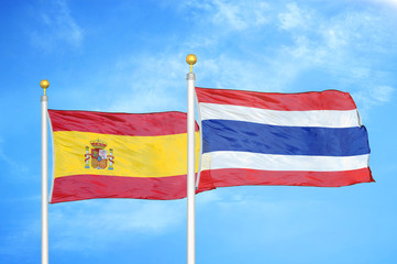 Spain and Thailand two flags on flagpoles and blue cloudy sky