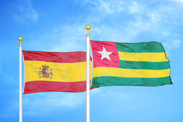 Spain and Togo two flags on flagpoles and blue cloudy sky