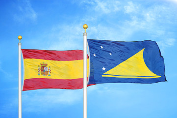 Spain and Tokelau two flags on flagpoles and blue cloudy sky