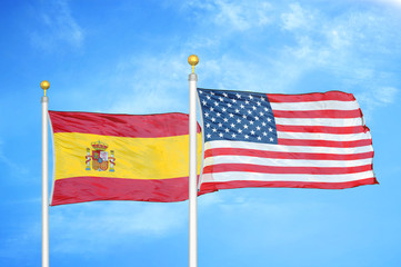 Spain and United States two flags on flagpoles and blue cloudy sky