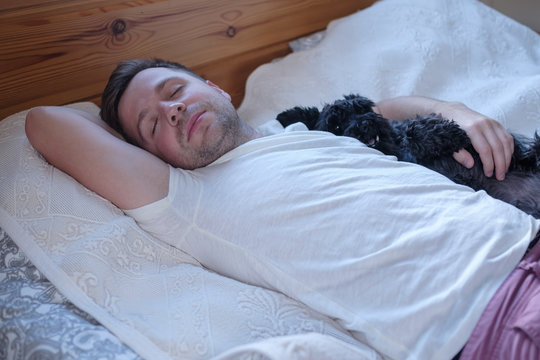 Young caucasian man sleeping in bed hugging his dog. Stay home.