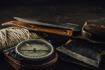 Old military compass, rusty hunting bushcraft knife, small axe and a linen rope on the dark wooden...