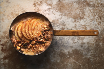 Overhead of Oatmeal with Apple Slices and Granola in Copper Pot