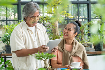 Relaxing Asian senior couple man and woman enjoy using digital tablet for reading news or social...