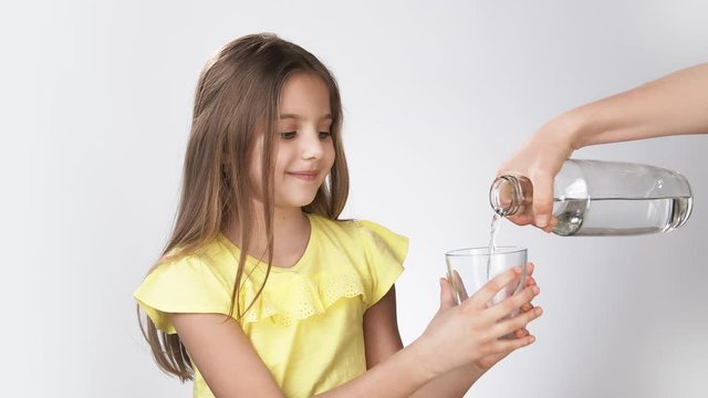 Mom pours water into a little girl's glass. little girl pours water into a glass. a girl in a yellow dress on a white background drinks water.