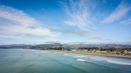Ocean, beach, surfers and blue sky. Aerial shot made in New Brighton Beach in Christchurch, New Zealand - obrazy, fototapety, plakaty
