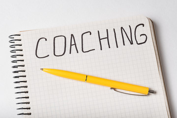 COACHING, word written on notebook. Top view of notepad and pen. Close up