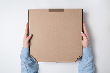 Female hands holding a cardboard box for pizza on white background. Top view, copy space, backdrop pattern