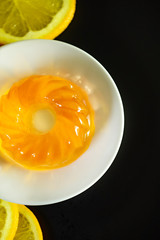vertical photo of yellow jelly on a black background and orange slices on the side of the frame. the view from the top