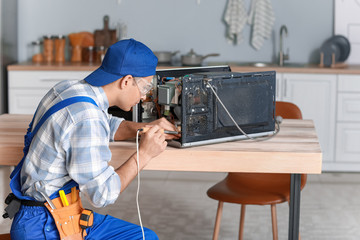 Worker repairing microwave oven in kitchen