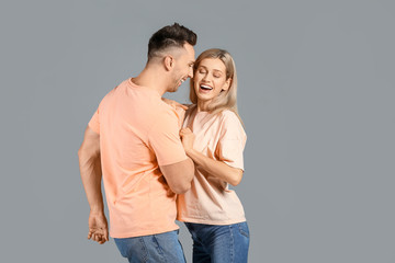 Fototapeta premium Happy young couple laughing together, joyful relationship and emotional connection, casual attire on gray background