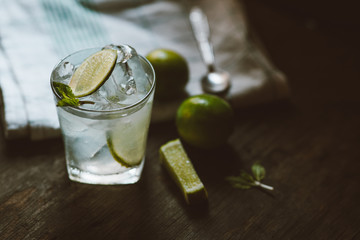 Handmade mojito cocktail with lime and mint leaves in glass on wood background at home. Vintage tone style