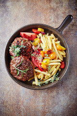 Fried hamburger steaks with tomatoes and french fries. Rustic background. Top view.	