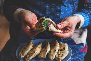 Homemade baked bread. Pie with potato and green spinach. Pirozhki - Russian traditional baked small pies. Woman hands. Vegan snack, vegetarian food. Dark style photo