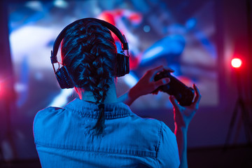 Young girl in headphones plays a video game on a screen projector or TV in the room. Gamer with a...