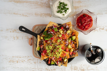 Corn nachos chips topped with ground beef, melted cheddar cheese, and guacamole on white wooden...