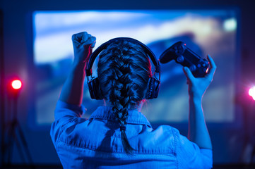 Gamer plays a video game on a TV or PC screen. Girl with a joystick and headphones in a neon room....