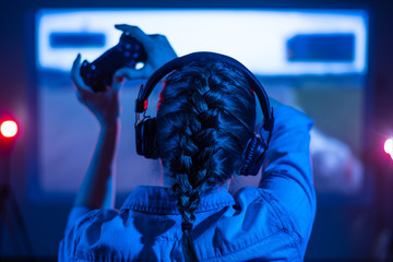 Gamer plays a video game on a TV or PC screen. Girl with a joystick and headphones. Online gaming,...