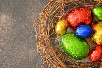 Nest with sweet chocolate eggs on grey background