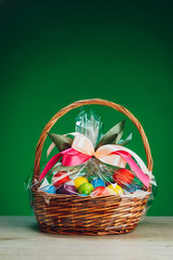 Fototapeta na wymiar Easter gift basket with multicolor eggs, green background