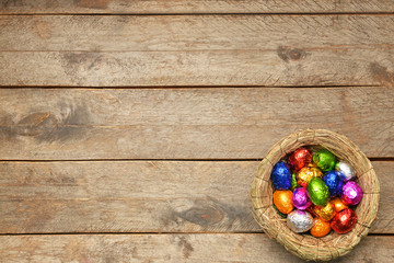 Nest with sweet chocolate eggs on wooden background