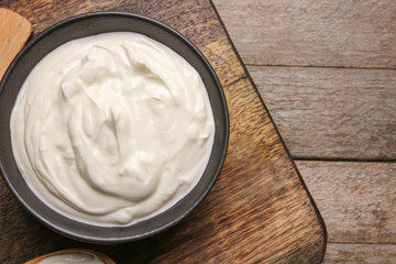 Bowl of tasty sour cream on wooden table