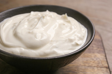 Obraz na płótnie Canvas Bowl of tasty sour cream on wooden table, closeup