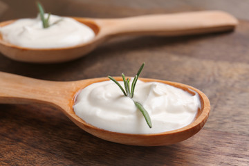 Spoons with tasty sour cream on wooden table, closeup