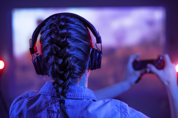 Funny teen gamer with headphones and a controller plays online computer and video games in a dark...