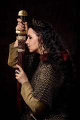A dark-haired woman with a sword and crown, a Scandinavian warrior in a chain mail against a dark background