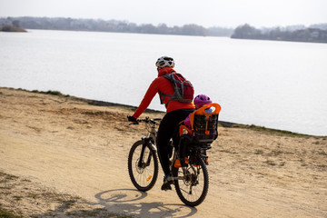 Fototapeta na wymiar Woman with baby on bike rides on sandy shore near water
