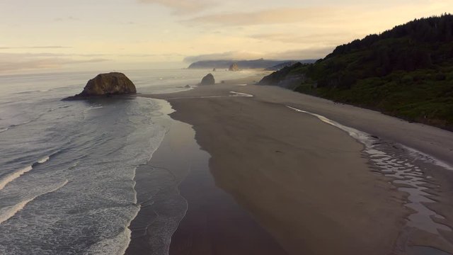 Aerial Tour of Cannon Beach, During a Beautiful Sunrise. As the sun rises a wonderful soft light illuminates the popular Haystack Rock in this much loved vacation destination. 