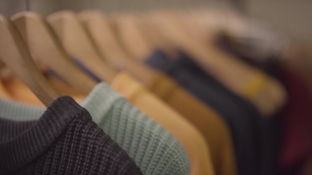 Close up shot with rack focus of colorful jumpers on hangers hanging on clothing rack