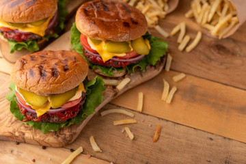 Grilled burger with beef, cheese, lettuce, onions, tomatoes, cucumbers and sauce. Homemade cooked cheeseburger on a wooden rustic table with french fries, salt and pepper