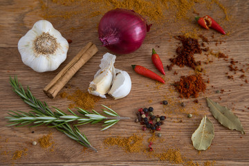A variety of spices, herbs, onion and garlic on a wooden service.