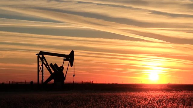 Silhouetted pumpjack in the oil field at sunset