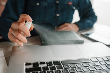 Coronavirus. Spray Sanitizer. Woman working in quarantine. Cleaning  keyboard of laptop computer to...