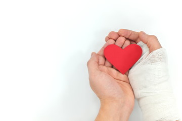 Injured hands holding red heart in white background. Selfless love, sacrifice and genuine kindness concept.