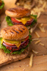 Hot cheeseburger on a wooden cutting board. Burger with beef, cheese, vegetables, crispy buns and salt fries on a rustic table. Fast food concept.