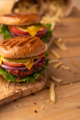 Hot juicy cheeseburger on a wooden cutting board. Burger with beef, cheese, vegetables, crispy buns and salt fries on a rustic table. Junk food concept.
