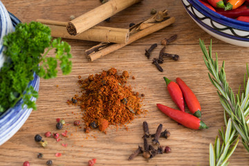 Cinamon sticks, chillies, peppers, cloves and other herbs and spices on a wooden service.  Parsley and chili in bowls.