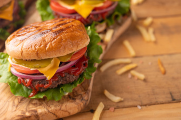 Hot cheeseburger on a wood cutting board. Homemade burger with beef, cheese, vegetables, crispy buns and salt fries on a rustic table. Fresh meat. Tasty meal. Restaurant menu. Cooking food concept.