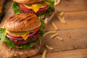 Hot juicy burger on a wooden cutting board. Cheeseburger with beef, cheese, vegetables, crispy buns and salt fries on a rustic table. Fresh meat. Tasty meal. Copy space